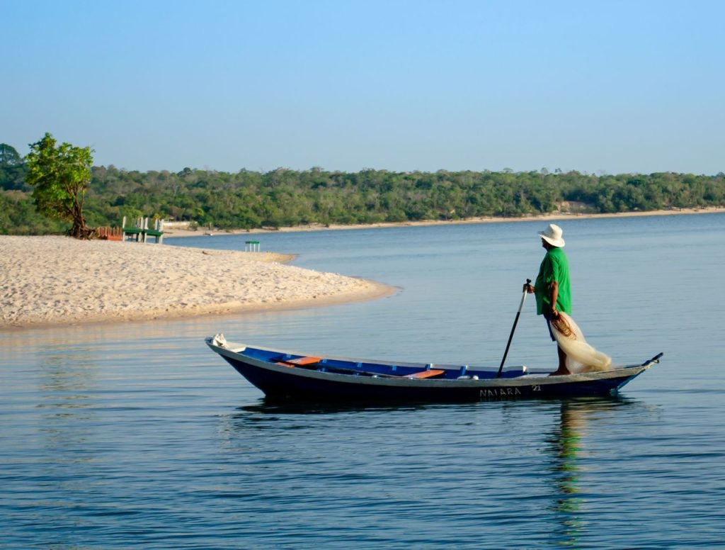 Pescador navega em uma canoa por um rio de águas tranquilas.