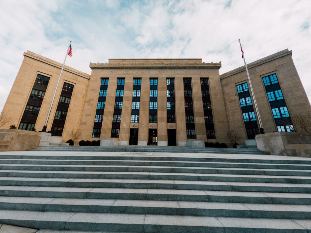 Exterior do prédio do Federal Reserve nos Estados Unidos, visto abaixo de bandeiras americanas e de uma escadaria.